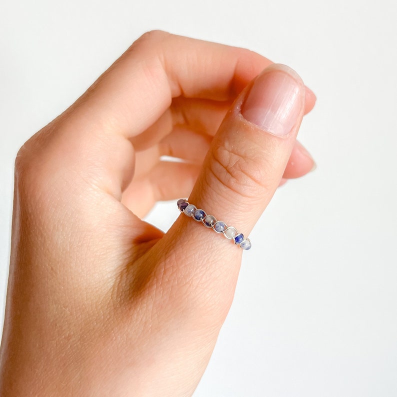May include: A silver ring with blue and white stones. The ring is worn on a person's thumb.