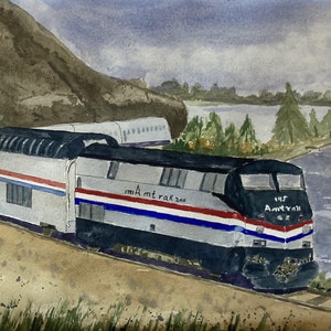 Peut inclure: Une peinture à l'aquarelle d'un train Amtrak argent et bleu qui roule sur un chemin de terre près d'une étendue d'eau. Le train est étiqueté "195 Amtrak" et "Amtrak 200".
