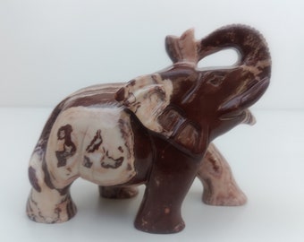 May include: A brown and white marble elephant figurine with its trunk raised. The elephant is carved from a stone with brown and white swirls.