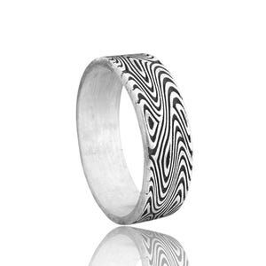 May include: A silver ring with a unique pattern of black and white wavy lines. The ring is displayed on a reflective surface, showcasing its design. The ring's band is thick and has a polished finish, making it a striking piece of jewelry.