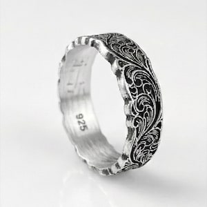 May include: A silver ring with an intricate floral pattern. The ring has a textured edge and the number "925" is visible on the inside. The design features swirling leaves and vines, creating a detailed and elegant look.