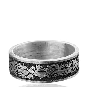 May include: A silver ring with a detailed floral pattern. The ring features a dark, textured band with an intricate design of leaves and vines. The ring's surface reflects light, highlighting the detailed craftsmanship.