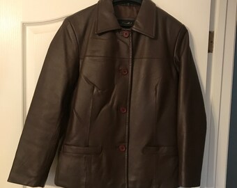 May include: A brown leather jacket with a button closure and two pockets. The jacket has a collar and long sleeves.