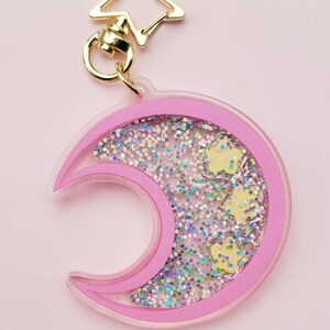 Pu&ograve; includere: Portachiavi a forma di mezzaluna rosa con glitter e stelle dorate all'interno. Il portachiavi ha una chiusura a forma di stella dorata.