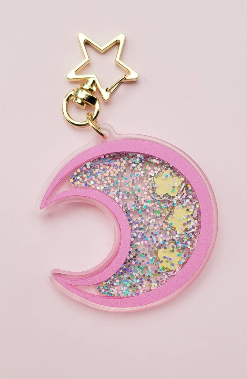 Pu&ograve; includere: Portachiavi a forma di mezzaluna rosa con glitter e stelle dorate all'interno. Il portachiavi ha una chiusura a forma di stella dorata.