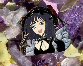 Può includere: Uno spillo in smalto bianco e nero con un personaggio in stile anime con capelli viola, che indossa un vestito nero con un colletto bianco e argento e una catena argentata. Il personaggio ha una fascia nera con un fiocco rosso e un choker argentato.