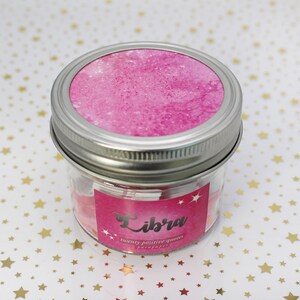 May include: A glass jar with a pink lid and a pink label that says "Libra twenty positive quotes for paper". The jar is sitting on a white background with gold stars.