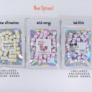 May include: Three white holographic pouches containing small white paper scrolls tied with colored rubber bands. The labels read swear affirmations, manifest that shit, witch energy, witch magic, bad b!tch, and includes uncensored swear words.