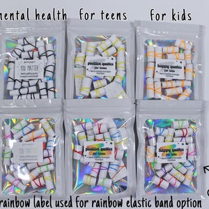 May include: Six clear holographic pouches containing rolled paper scrolls secured with elastic bands. Labels read: mental health, you matter, positive quotes for teens, happy quotes for kids, and rainbow label used for rainbow elastic band option.