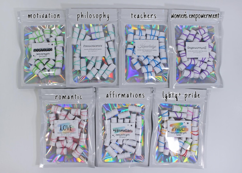 May include: Seven holographic pouches containing small white paper scrolls tied with colored elastic bands. Each pouch features a label with themes including motivation, philosophy, teachers, women's empowerment, romantic, affirmations, and lgbtq+ pride.