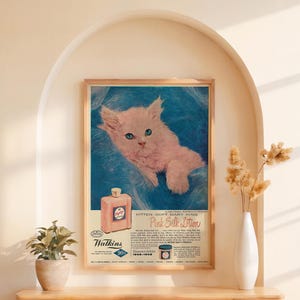May include: Vintage advertisement for Watkins Pink Silk Lotion featuring a white kitten with blue eyes on a blue background. The text reads "Kitten Soft Mary King Pink Silk Lotion".
