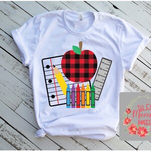 K&ouml;nnte beinhalten: Wei&szlig;es T-Shirt mit einem Schul-Themen-Design. Die Grafik zeigt einen rot-schwarz karierten Apfel, einen gelben Bleistift, ein Lineal, einen Notizblock und ein Set Buntstifte. Das T-Shirt hat einen Rundhalsausschnitt und kurze &Auml;rmel.