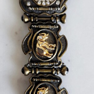 May include: Vintage gold-toned watch with a decorative band. The watch face is surrounded by clear crystals. The band features gold elephant figures set in ornate frames. The watch has a quartz movement.