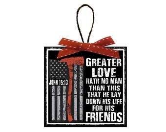 Può includere: Un ornamento quadrato nero con un designo di bandiera americana rosso, bianco e blu e il testo "JOHN 15:13" e "GREATER LOVE HATH NO MAN THAN THIS THAT HE LAY DOWN HIS LIFE FOR HIS FRIENDS".