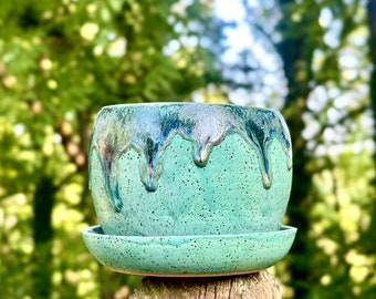 May include: A turquoise green ceramic planter with a drip glaze and a matching saucer. The planter has a speckled finish.