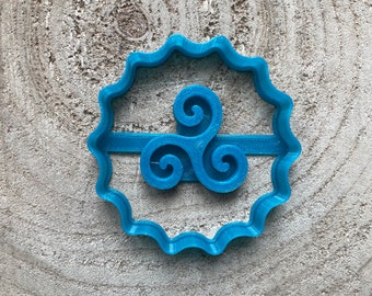 May include: A blue plastic cookie cutter shaped like a triskelion, a Celtic symbol with three interlocked spirals.