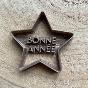 Peut inclure: Un emporte-pièce en forme d'étoile en plastique marron avec les mots "BONNE ANNÉE" en relief.