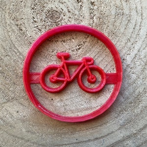 May include: Red plastic cookie cutter shaped like a bicycle. The bicycle has a simple design with two wheels, handlebars, and a seat.