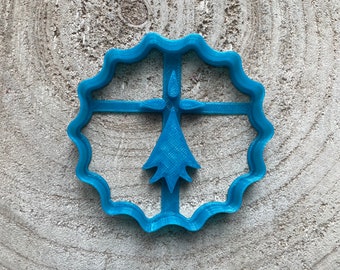 May include: A blue plastic cookie cutter shaped like a stylized Christmas tree with a star on top. The cutter has a wavy edge.