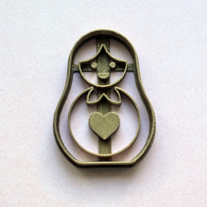Peut inclure: Un emporte-pièce en métal de couleur dorée en forme de poupée russe traditionnelle, ou matriochka, avec un cœur au centre.