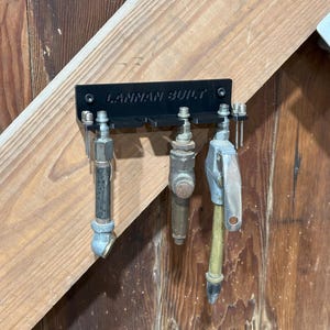 May include: A black plastic wall-mounted air hose holder with the text "LANMAN BUILT" printed on it. Three air hoses are hanging from the holder.