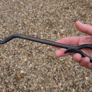 May include: A black metal fireplace poker with a curved handle and a hook at the end. The poker is designed for moving logs in a fireplace.
