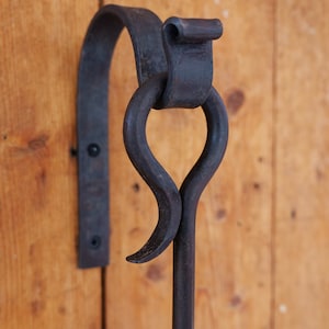 May include: A black metal hook with a decorative loop, mounted on a wooden wall.