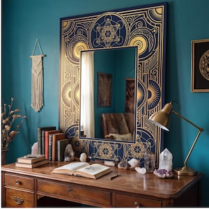 May include: A rectangular wall mirror featuring a dark navy blue frame adorned with intricate gold geometric patterns, including sacred geometry motifs. The mirror reflects a room interior, showcasing a clear glass surface surrounded by detailed gold linework.
