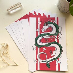 May include: A stack of white cards with a red background featuring a white and green dragon with white crosses on the red background.