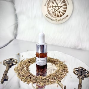 Può includere: Un piccolo flacone di vetro con un tappo argentato e un contagocce. Il flacone è riempito con un liquido rosso-marrone e ha un'etichetta che recita "Road Opener". Il flacone è appoggiato su un vassoio argentato con erbe secche e due chiavi.