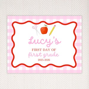 May include: A rectangular sign with a pink gingham pattern border and a red wavy frame. The sign features the text "Lucy's First Day of First Grade 2025-2026" in pink script. Illustrations of scissors, an apple, and a pencil are included.