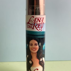 May include: A silver Clipper lighter with a white label featuring a photo of Lana Del Rey and the text "Lana Del Rey" and "Lust for Life".