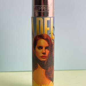 May include: A silver Clipper lighter with a colorful design featuring a portrait of Adele and the text "Born to Die".