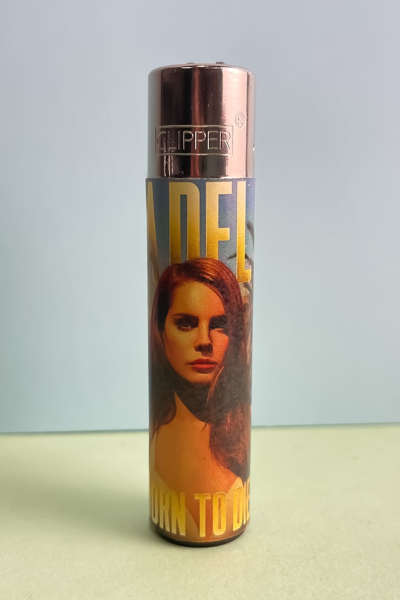 May include: A silver Clipper lighter with a colorful design featuring a portrait of Adele and the text "Born to Die".