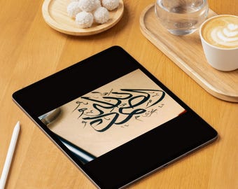 May include: A black tablet displays calligraphy art with a pen. A wooden tray holds a glass of water and a cup of coffee. A small wooden plate holds several white, round treats. The items are on a light brown wooden surface.