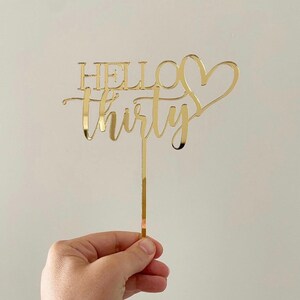 May include: Gold glitter cake topper with the text "Hello Thirty" and a heart.
