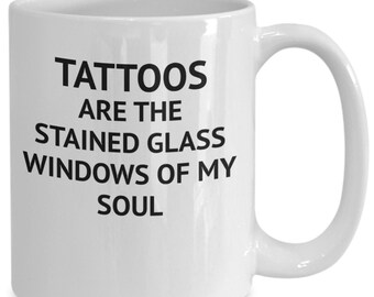 Könnte beinhalten: Eine weiße Keramik-Kaffeetasse mit schwarzem Text, der lautet: "Tattoos sind die Buntglasfenster meiner Seele."