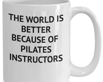 Op de afbeelding: Witte keramische koffiemok met zwarte tekst die "De wereld is beter vanwege Pilates-instructeurs" luidt.