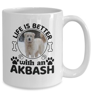 Puede incluir: Taza de café de cerámica blanca con un diseño gráfico en blanco y negro. El diseño presenta un perro blanco en un paisaje nevado con el texto "Life is better with an Akbash".