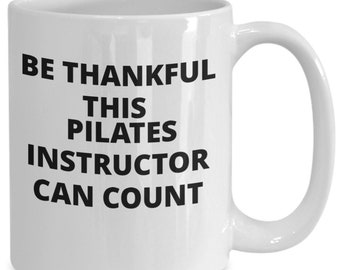 Op de afbeelding: Witte keramische koffiemok met zwarte tekst die "Be Thankful This Pilates Instructor Can Count" luidt.