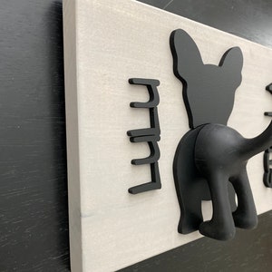 K&ouml;nnte beinhalten: Ein wei&szlig;er, an der Wand montierter Kleiderst&auml;nder mit schwarzen Silhouette-Haken in Form von Hunden. Der St&auml;nder hat f&uuml;nf Haken in Form eines Hunde-Schwanzes und eines Hunde-Kopfes.