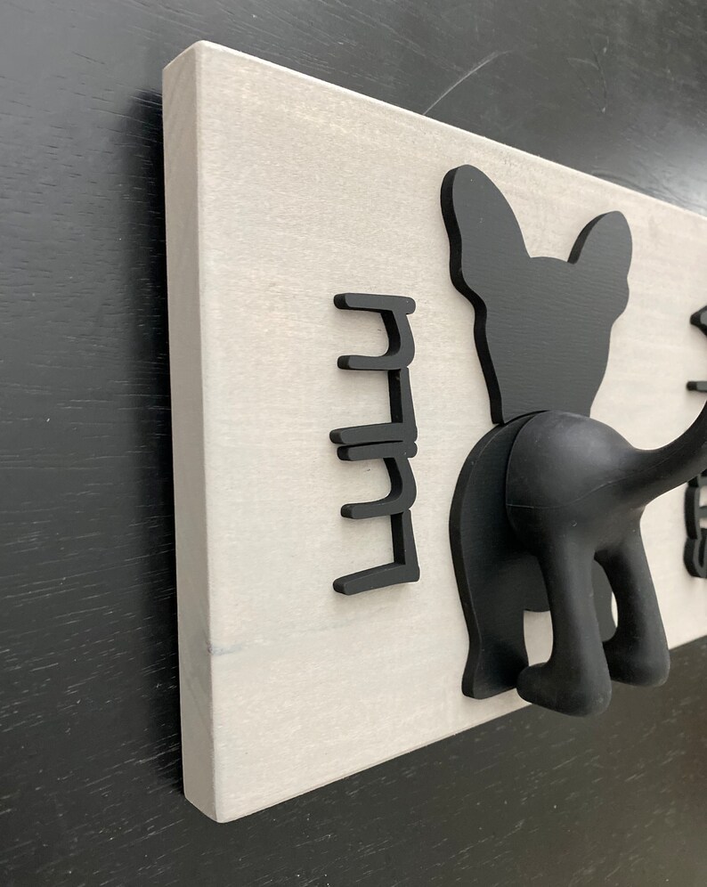 K&ouml;nnte beinhalten: Ein wei&szlig;er, an der Wand montierter Kleiderst&auml;nder mit schwarzen Silhouette-Haken in Form von Hunden. Der St&auml;nder hat f&uuml;nf Haken in Form eines Hunde-Schwanzes und eines Hunde-Kopfes.