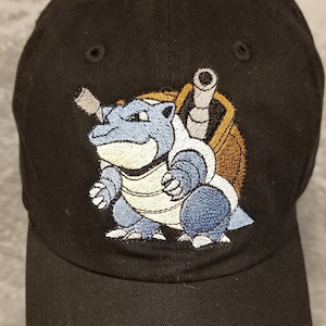 May include: Black baseball cap with an embroidered image of a blue and brown Pokemon character.