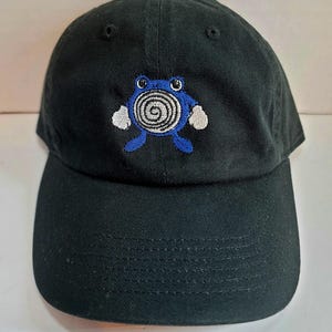 May include: Black baseball cap with an embroidered blue and white cartoon frog with a spiral on its belly.