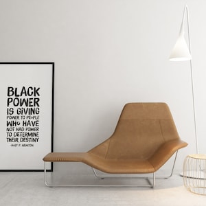 May include: Black and white framed print with the quote "Black Power is giving power to people who have not had power to determine their destiny -  W.E.B. Du Bois". The print is hanging on a white wall above a brown leather lounge chair.