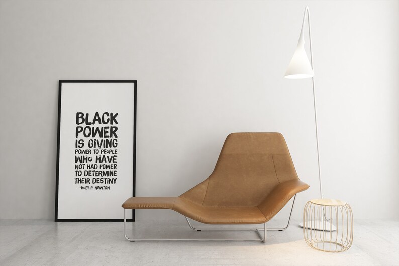 May include: Black and white framed print with the quote "Black Power is giving power to people who have not had power to determine their destiny -  W.E.B. Du Bois". The print is hanging on a white wall above a brown leather lounge chair.