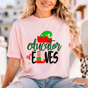 May include: Pink t-shirt with a green and red elf hat graphic and the text "educator of elves".