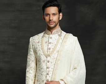 Puede incluir: Un sherwani blanco para hombre bordado con un dupatta blanco a juego. El sherwani tiene un diseño bordado en dorado y un collar de perlas. El dupatta tiene un borde bordado en dorado.