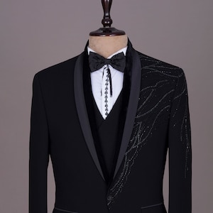 May include: A black tuxedo jacket with a velvet lapel and a black bow tie. The jacket features a decorative design of black sequins on the front and sleeves.