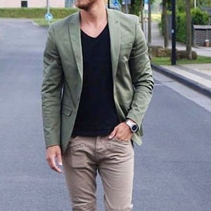 Puede incluir: Un hombre con una chaqueta verde, una camiseta negra, pantalones caqui y zapatillas blancas.